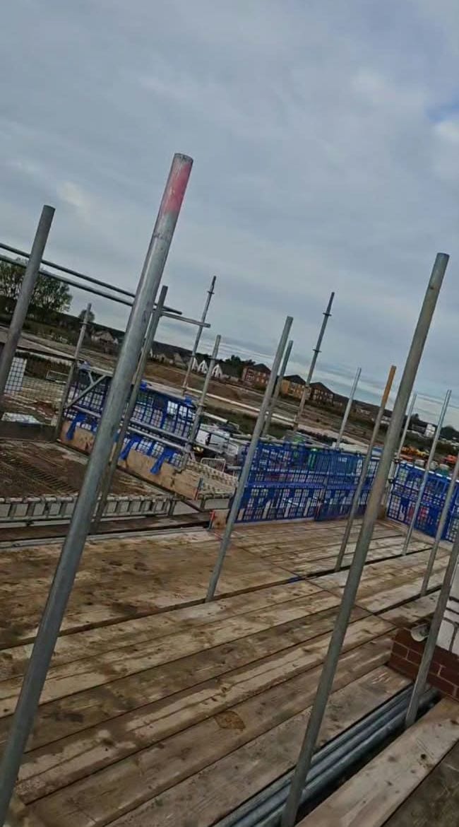 Looking along a boarded working lift, with standards and blue brick guards against a cloudy sky