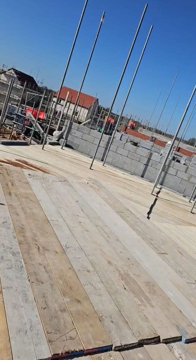 Scaffold boards laid tight on a working lift in bright sun, with standards rising past a blockwork wall