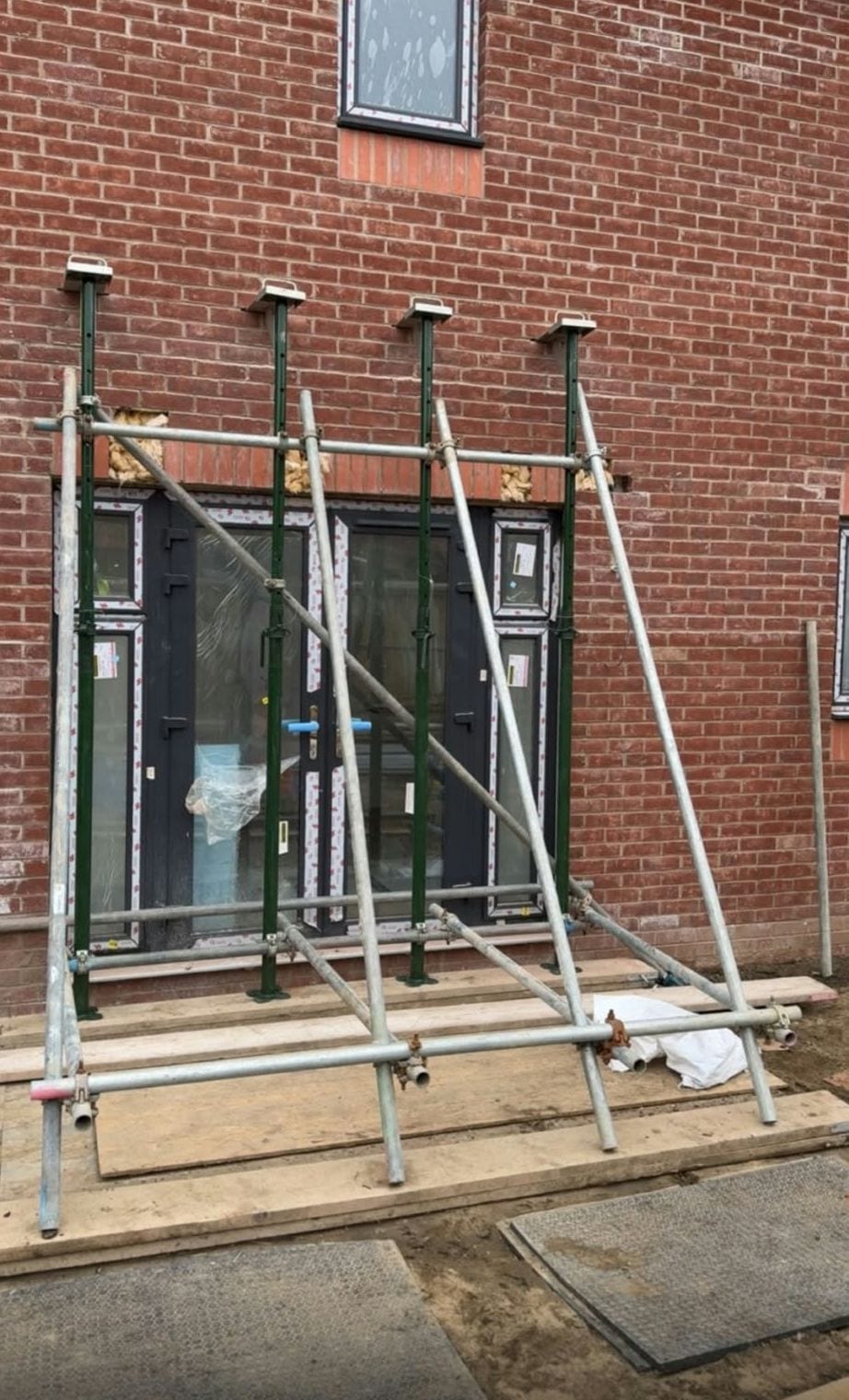 Tube and fitting frame with raking braces standing around a pair of French doors in a brick wall