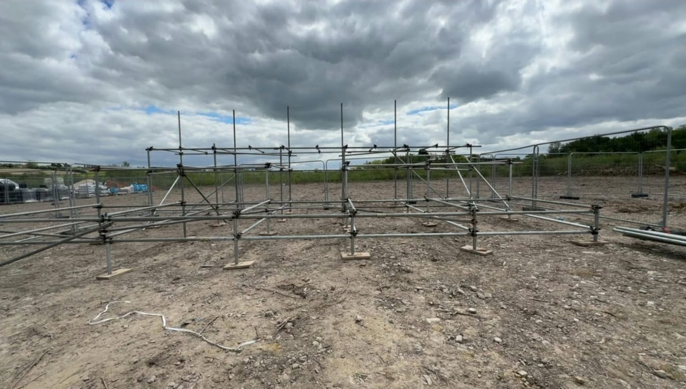 The base of a scaffold set out on sole boards across a cleared plot, standards up and the first ledgers on