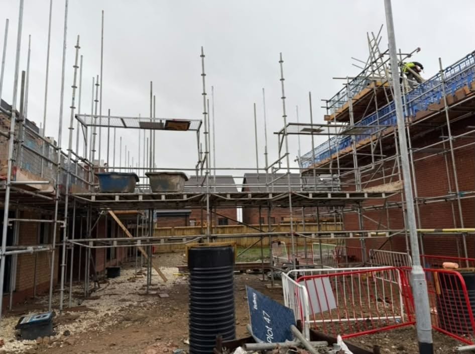 A row of new brick houses under scaffold on a building site, with standards standing above the roofline